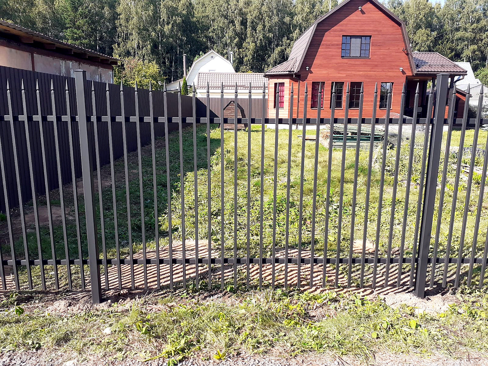 Металлическое ограждение с прямыми вертикалями перед красным загородным домом